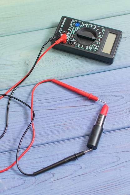 Multimeter misst roten Lippenstift auf Holzhintergrund Das Konzept zur Messung des Einflusses von Lippenstift