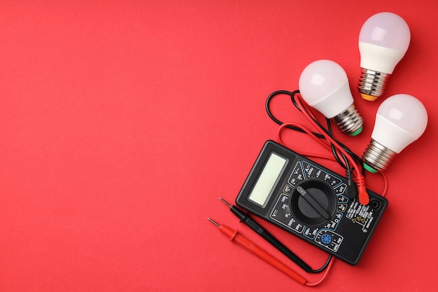 Multimeter und Energiesparlampen auf rotem Hintergrund