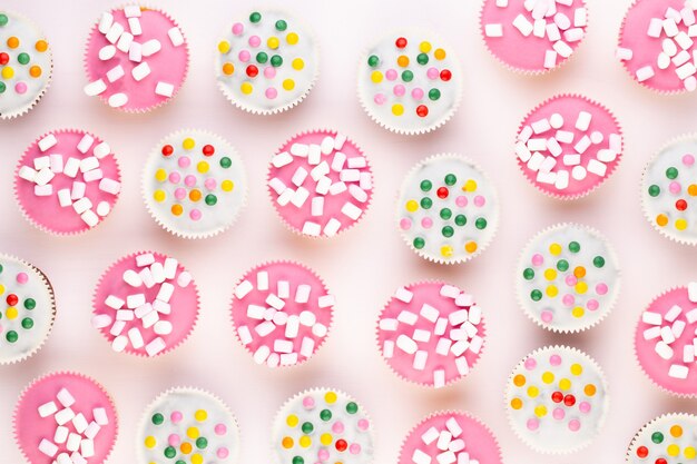 Múltiples muffins de colores muy bien decorados sobre un fondo blanco, vista superior.