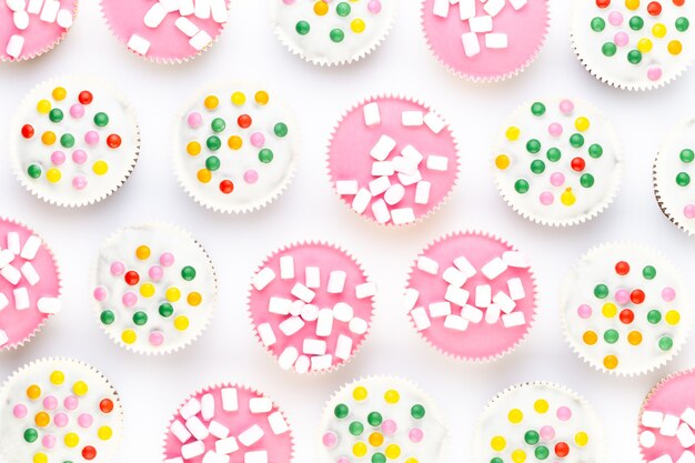 Múltiples muffins de colores muy bien decorados sobre un fondo blanco.
