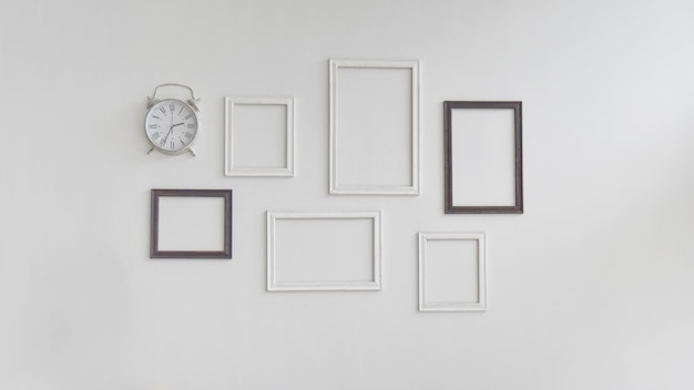 Múltiplos quadros em branco e relógio em fundo branco da parede