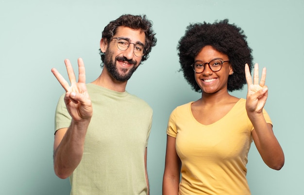 Multirassische Freunde, die lächeln und freundlich aussehen, die Nummer drei oder drei mit der Hand nach vorne zeigen und herunterzählen