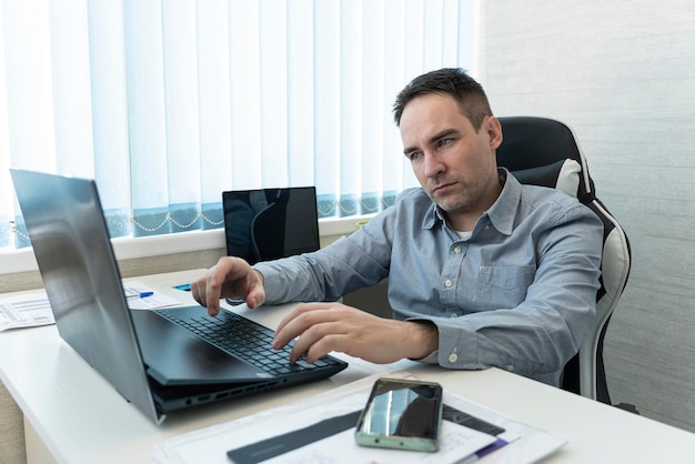 Multitasking-Geschäftsmann, der im Büro arbeitet Er benutzt das Touchpad, während er eine E-Mail auf dem Laptop liest