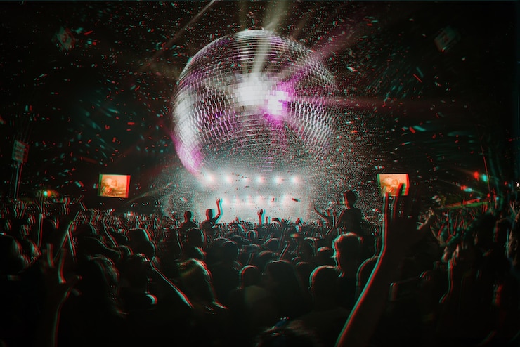 Foto multitud en un festival bailando con las manos en alto y una bola de discoteca gigante con efecto de falla