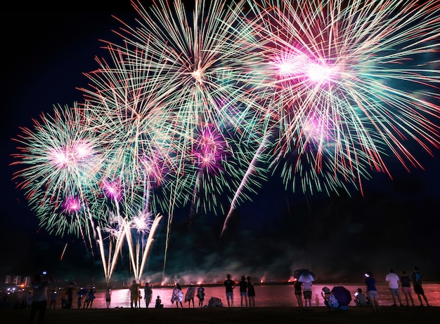 Foto multitud viendo fuegos artificiales en la playa.