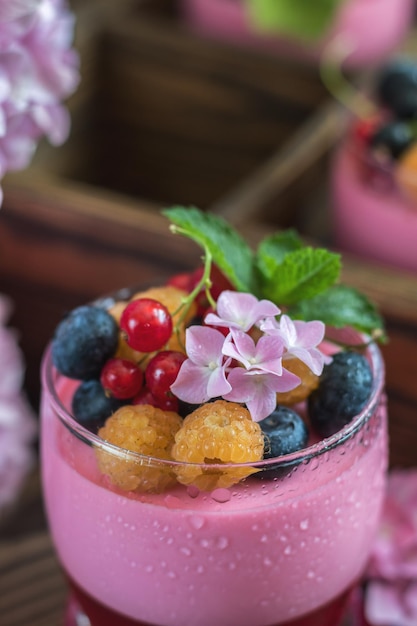 Multivitamin-Sommerbeere, köstliche Panacotta, süßes Essen mit Himbeeren, Blaubeeren, Johannisbeeren, Croutons und mintrosa Hortensienstrauß, dunklem Holzhintergrund