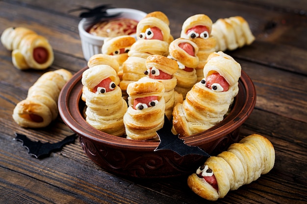 Múmias assustadores da salsicha na massa com os olhos engraçados na tabela. Decoração engraçada. Comida de Halloween.