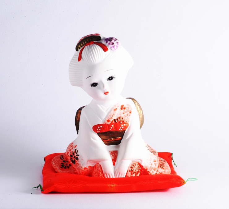 Muñeca japonesa de cerámica vestida con kimono sentada en una almohada naranja brillante