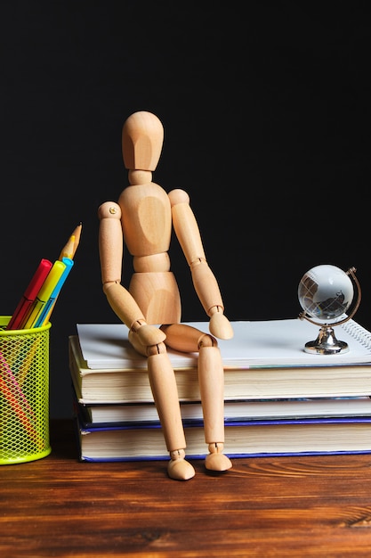 Muñeca de madera sentada en los libros y papelería.