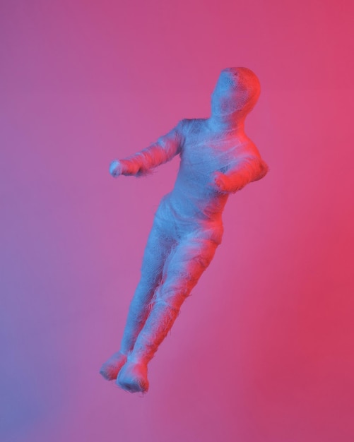 Muñeca momia flotando en el aire aislada en luz de neón azulado objetos levitantes concepto minimalista de Halloween