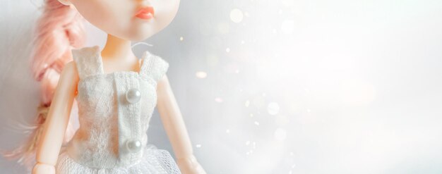 Una muñeca con un vestido blanco con cabello rosado se destaca contra un formato de banner de fondo bokeh mágico