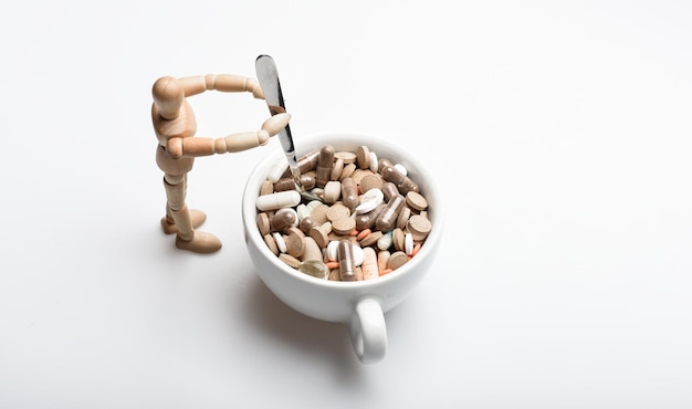 Muñeco humano de madera cerca de la taza llena de pastillas y tabletas Tomar el concepto de medicina Cóctel de vitaminas Problema de salud Inmunidad y medicina vitaminas Mezcla de medicamentos Tratamiento rápido Prescripción de medicamentos