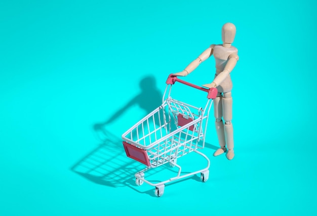 Muñeco de madera con un mini carrito de compras sobre un fondo turquesa