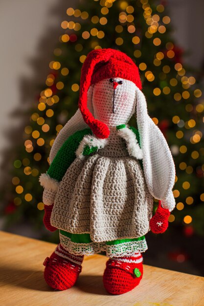 Muñeco de Navidad de ganchillo está de pie sobre una mesa de madera contra el fondo de un árbol de Navidad