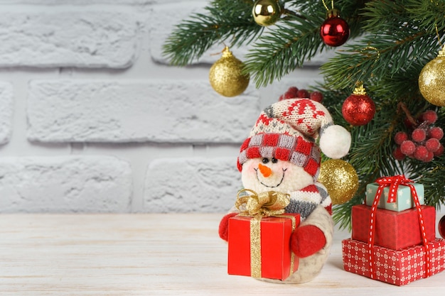 Muñeco de nieve de año nuevo con caja de regalo roja sobre fondo de árbol de Navidad decorado