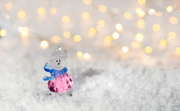 Muñeco de nieve de cristal en la nieve con luces borrosas en el fondo. El concepto de celebración.
