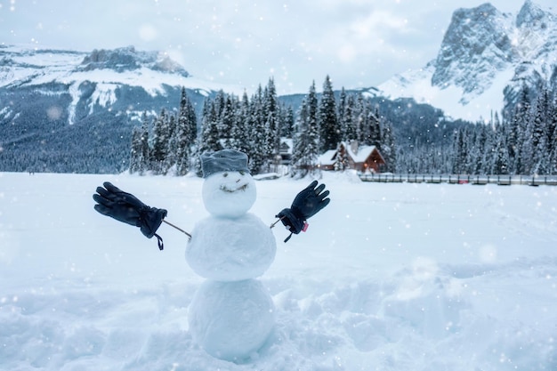 Muñeco de nieve feliz con gorro y guante en invierno en el fondo del pueblo de la casa de madera