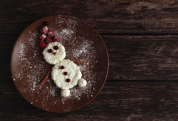 Muñeco de nieve hecho de requesón y frambuesas y arándanos rojos en un plato marrón sobre un fondo de madera