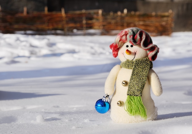 Muñeco de nieve de juguete con juguete de Navidad en manos de pie en la nieve