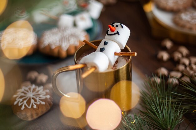 Un muñeco de nieve de malvavisco decorado con glaseado taza de oro con cacao y decoración navide ...