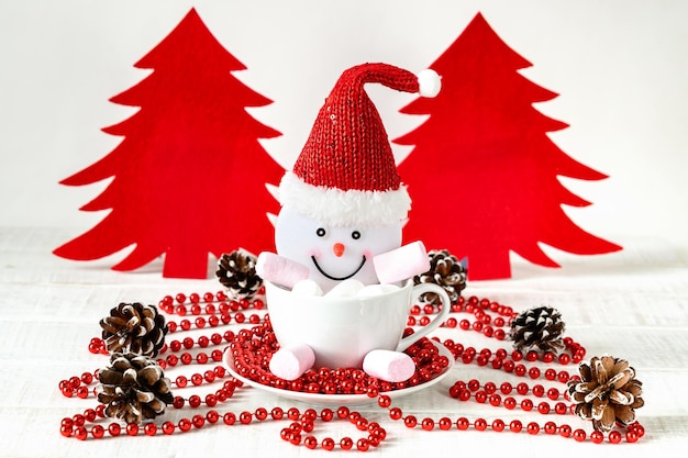 Muñeco de nieve y malvaviscos en taza árbol de Navidad de fieltro rojo sobre mesa blanca