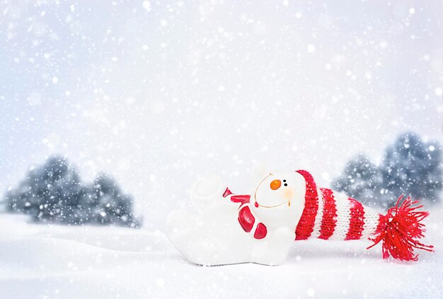 Un muñeco de nieve con un sombrero rojo yace en la nieve bajo la nieve que cae