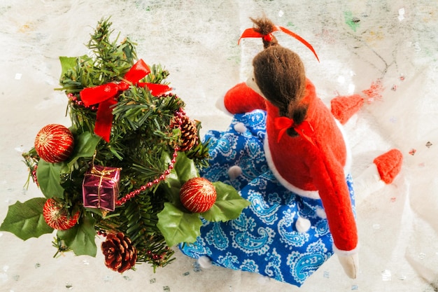 Muñeco textil suave cerca de un árbol de Navidad con regalos