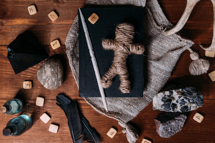 Foto un muñeco vudú hecho de cuerda yace sobre un libro negro, rodeado de objetos rituales mágicos, plano