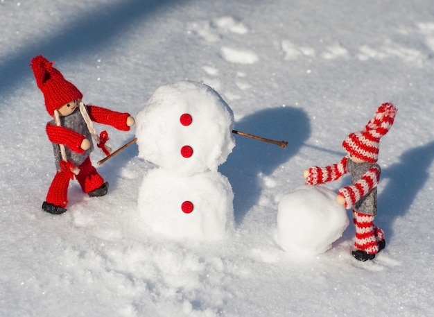 muñecos de madera con ropa de punto rojo ruedan bolas de nieve para construir un muñeco de nieve