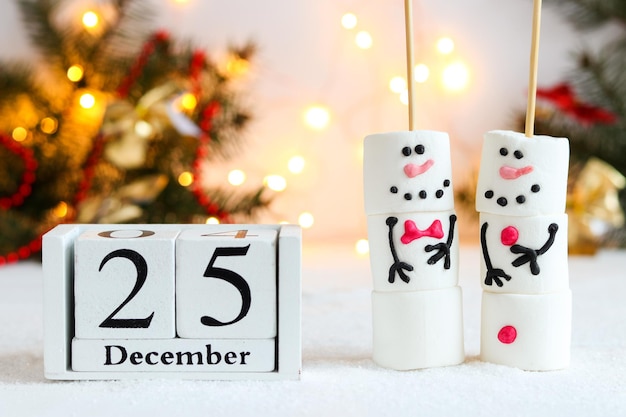 Muñecos de nieve de malvavisco y calendario con fecha del 25 de diciembre contra las decoraciones festivas de invierno