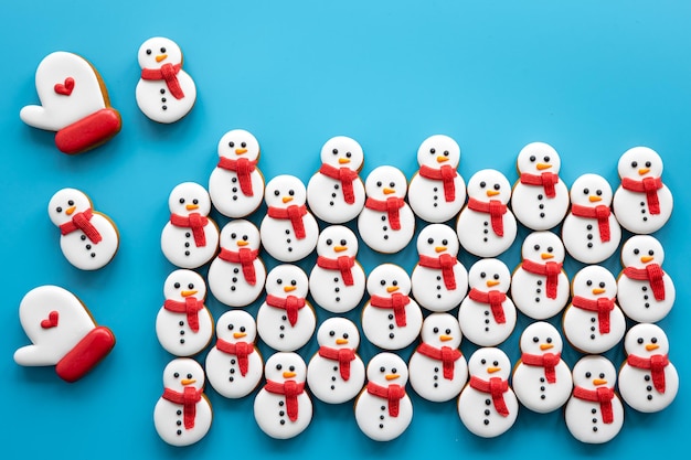 Muñecos de nieve de pan de jengibre cubiertos con glaseado sobre un fondo azul plano