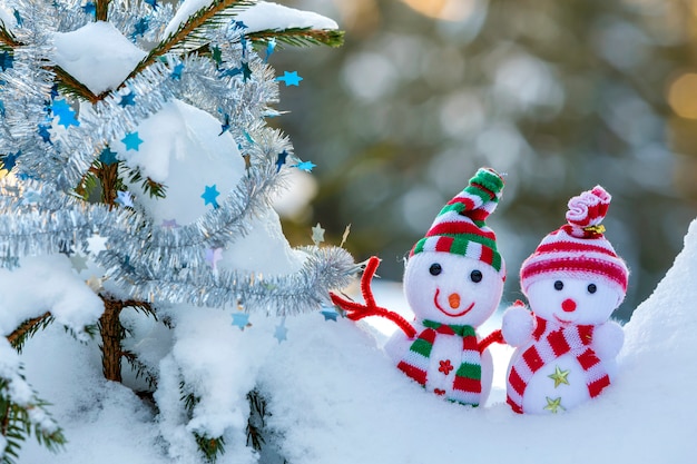 muñecos de nieve con sombreros de punto y bufandas en la nieve profunda cerca de la rama de pino.