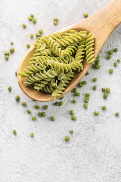 Foto mung-bohnen-fusilli-pasta auf einem grauen beton-hintergrund löffel mit roher pasta und grüner mung-bohn-glutenfreie pasta