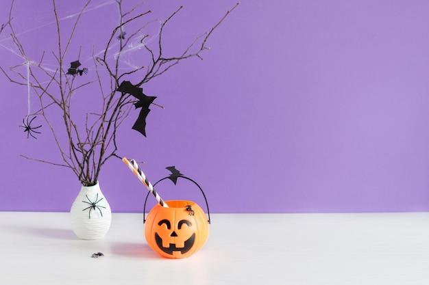 Murciélagos de papel de decoraciones de Halloween volando en rama de árbol y cubo de calabaza en la mesa.