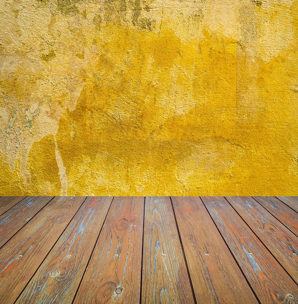 Foto muro de cemento amarillo dañado con piso de madera marrón