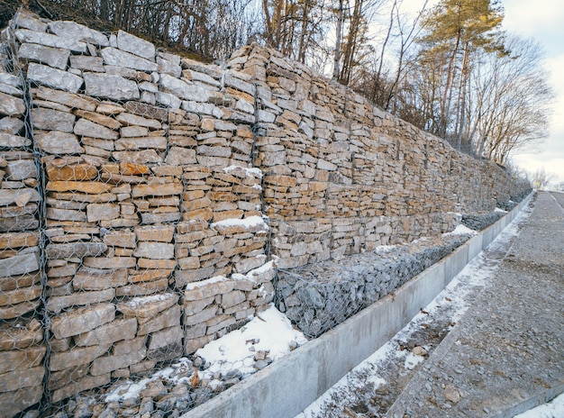 Muro de gaviones de piedra a lo largo de la carretera asfaltada en invierno