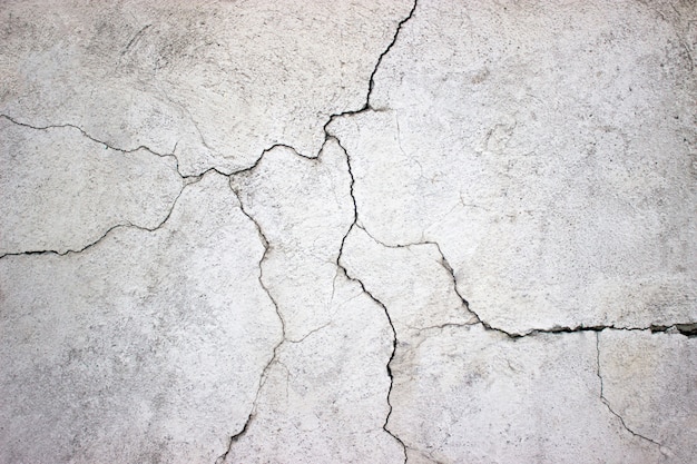 Muro de hormigón agrietado cubierto con textura de cemento gris como fondo para el diseño