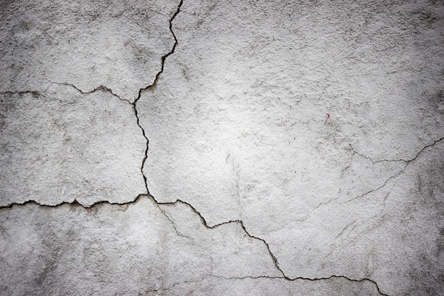 Muro de hormigón agrietado cubierto con textura de cemento gris como fondo para el diseño