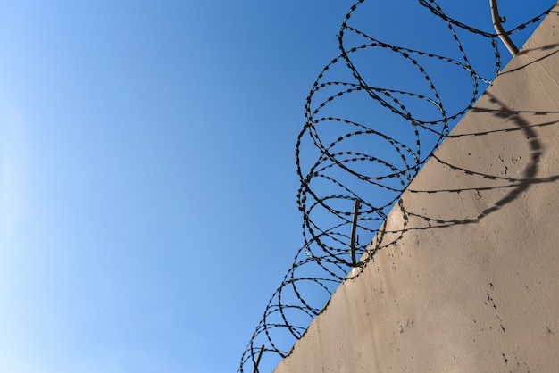 Muro de la prisión con alambre de púas contra el cielo azul