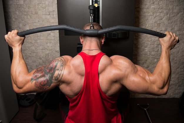 Muscular atlético culturista modelo de fitness haciendo ejercicio de peso pesado para la espalda en la máquina