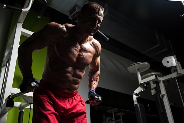 Muscular Fitness culturista haciendo ejercicio de peso pesado para tríceps y pecho en barras paralelas en el gimnasio