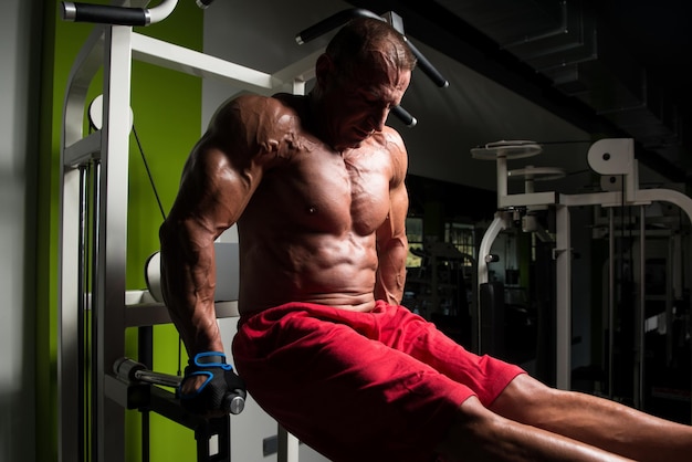 Muscular Fitness culturista haciendo ejercicio de peso pesado para tríceps y pecho en barras paralelas en el gimnasio