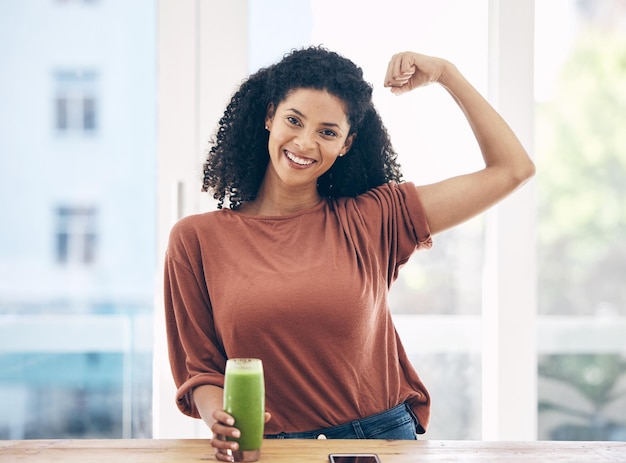 Foto músculo de retrato e smoothie com uma mulher negra na cozinha de uma casa flexionando seu bíceps para saúde perda de peso de bem-estar e forte com uma jovem atraente bebendo uma bebida dietética