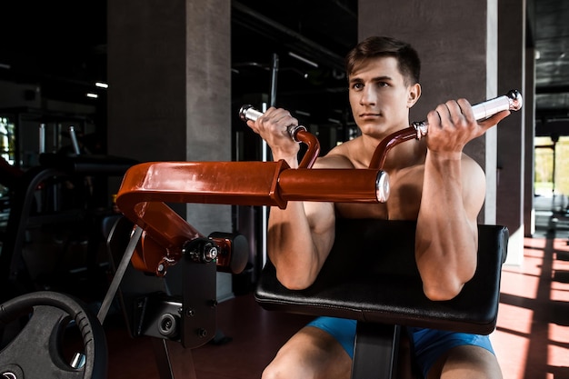 Los músculos tensos de las manos bajo carga. Hombre haciendo ejercicio para los bíceps en el gimnasio. Trabajar en los músculos de la palanca en el simulador. Fotos para revistas deportivas, carteles y sitios web.