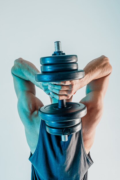 Músculos tríceps de treinamento de desportista com halteres. vista traseira do homem usar uniforme esportivo. isolado em fundo turquesa. sessão de estúdio