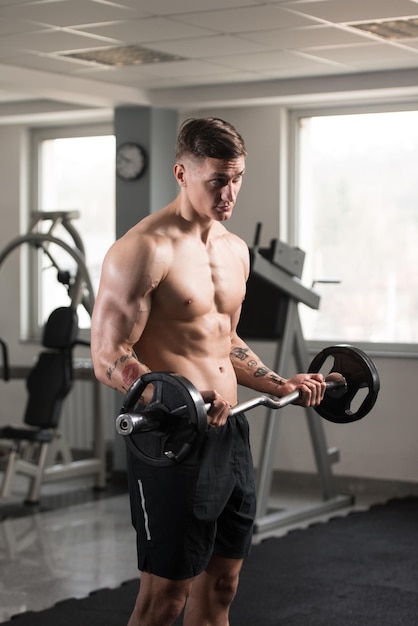 Musculoso jovem exercitando bíceps com barra