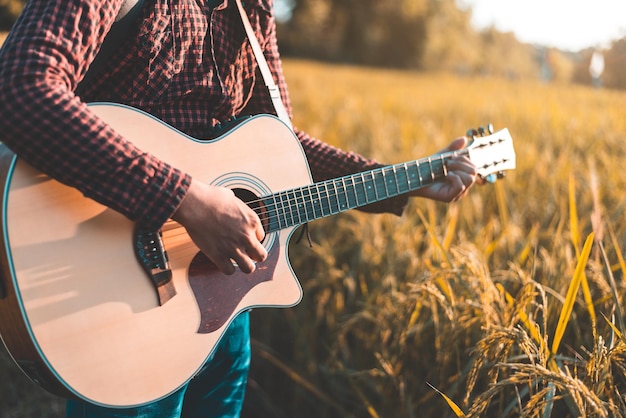 Música country Homem tocando violão no campo de arroz Foco nas cordas da guitarra