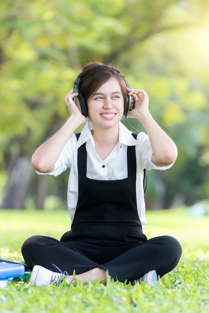 Música de escuta asiática da jovem mulher do leitor de mp3 no parque do verão.