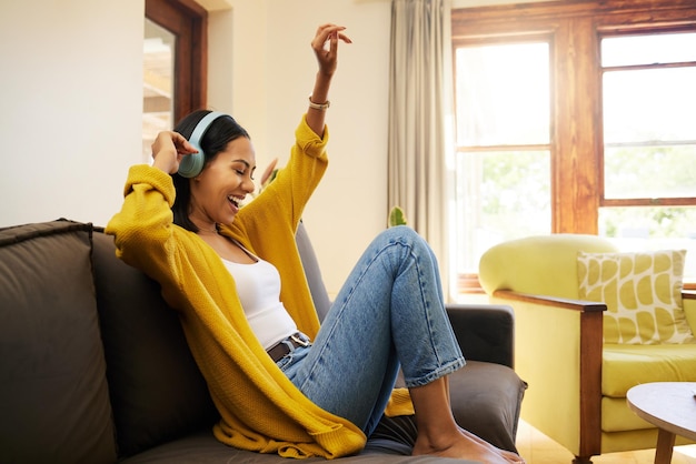 Foto música de mulher e relaxe com fones de ouvido dançando no sofá da sala desfrutando de boas vibrações em casa mulher feliz com sorriso e dança ouvindo streaming de áudio alegre relaxando em um sofá em casa