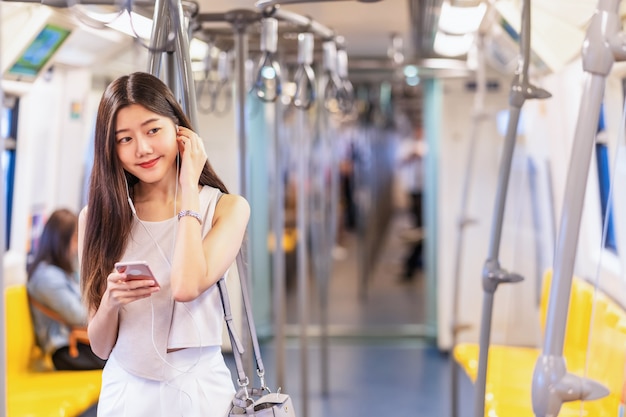 Música de passageiro jovem mulher asiática através do telefone móvel esperto no trem do metrô quando viaja na cidade grande, japonês, chinês, estilo de vida coreano e conceito de vida diária, viajante e transporte